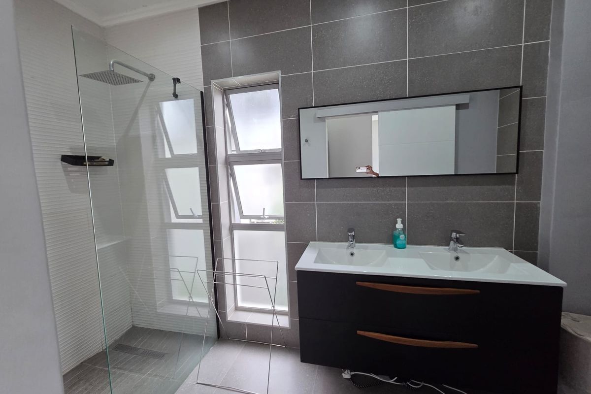 Modern bathroom featuring a double vanity with dark cabinetry, a spacious walk-in shower with a rain shower head, and contemporary grey wall tiling.