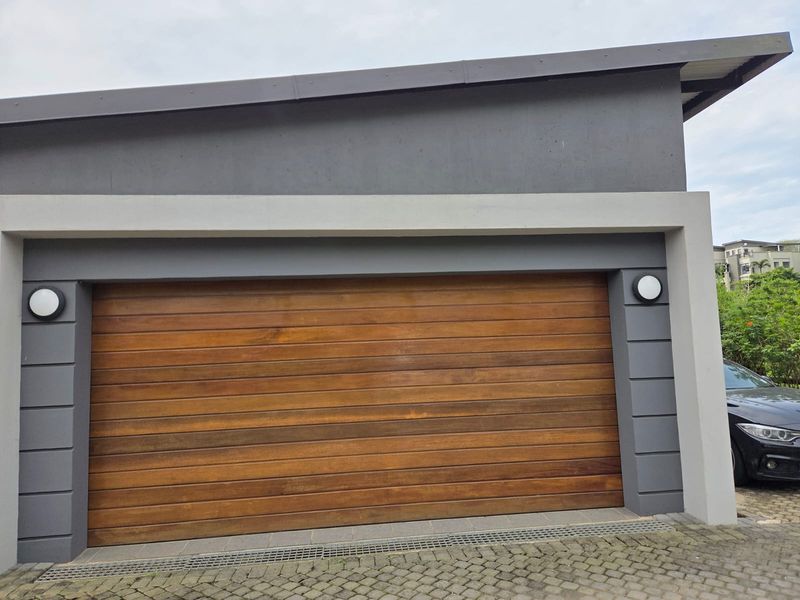 Modern garage exterior featuring a high-quality timber sectional door, clean grey rendered facade, and paved driveway with integrated drainage.