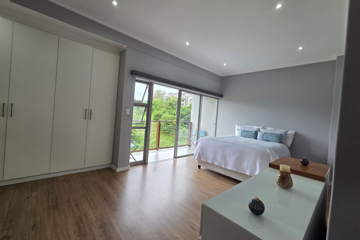 Spacious bedroom featuring modern laminate flooring, built-in cupboards, recessed lighting, and large sliding glass doors opening onto a private balcony with scenic views.