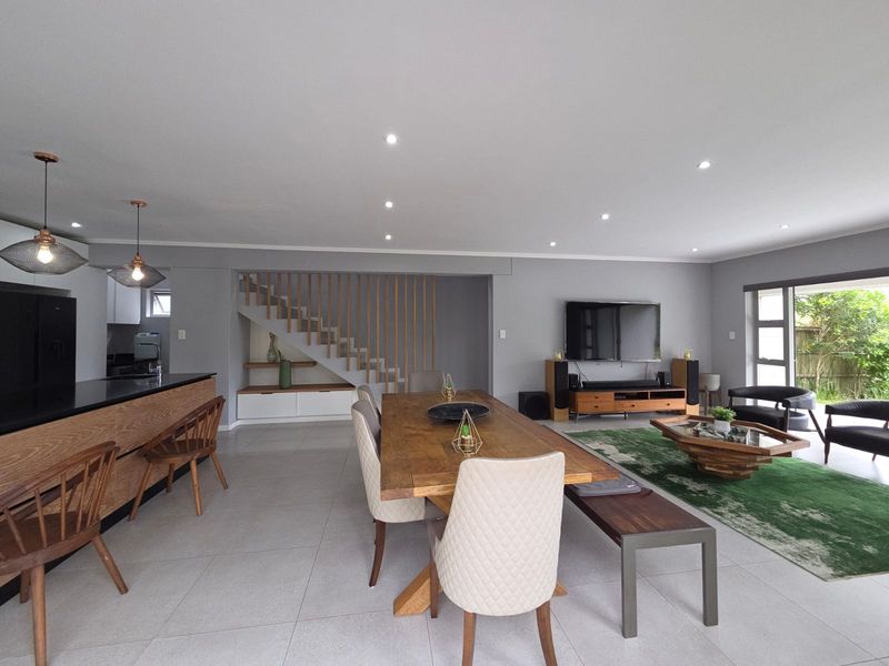 Spacious open-plan living and dining area featuring a modern kitchen island, timber staircase with slat detailing, and seamless access to the outdoor space.