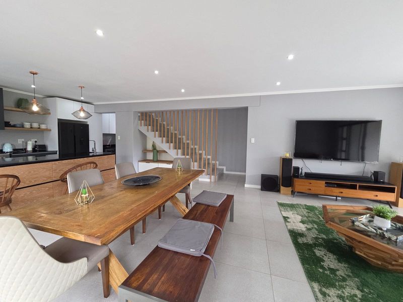 Modern open-plan living area featuring a contemporary kitchen, dining space, and a striking timber staircase, all finished with neutral tones and tiled flooring.