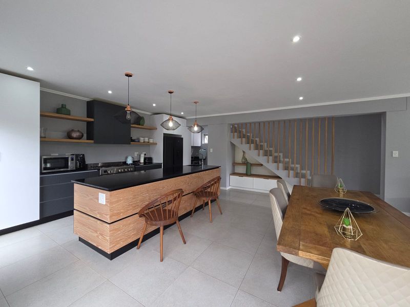 Modern open-plan kitchen and dining area featuring a timber-accented island, sleek cabinetry, integrated appliances, and a contemporary staircase with timber balustrades.