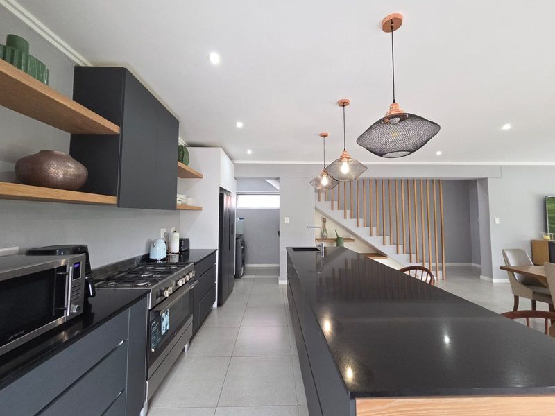 Modern open-plan kitchen featuring a large island, dark cabinetry, stone countertops, gas cooktop, and stylish pendant lighting, seamlessly integrated with the living area.
