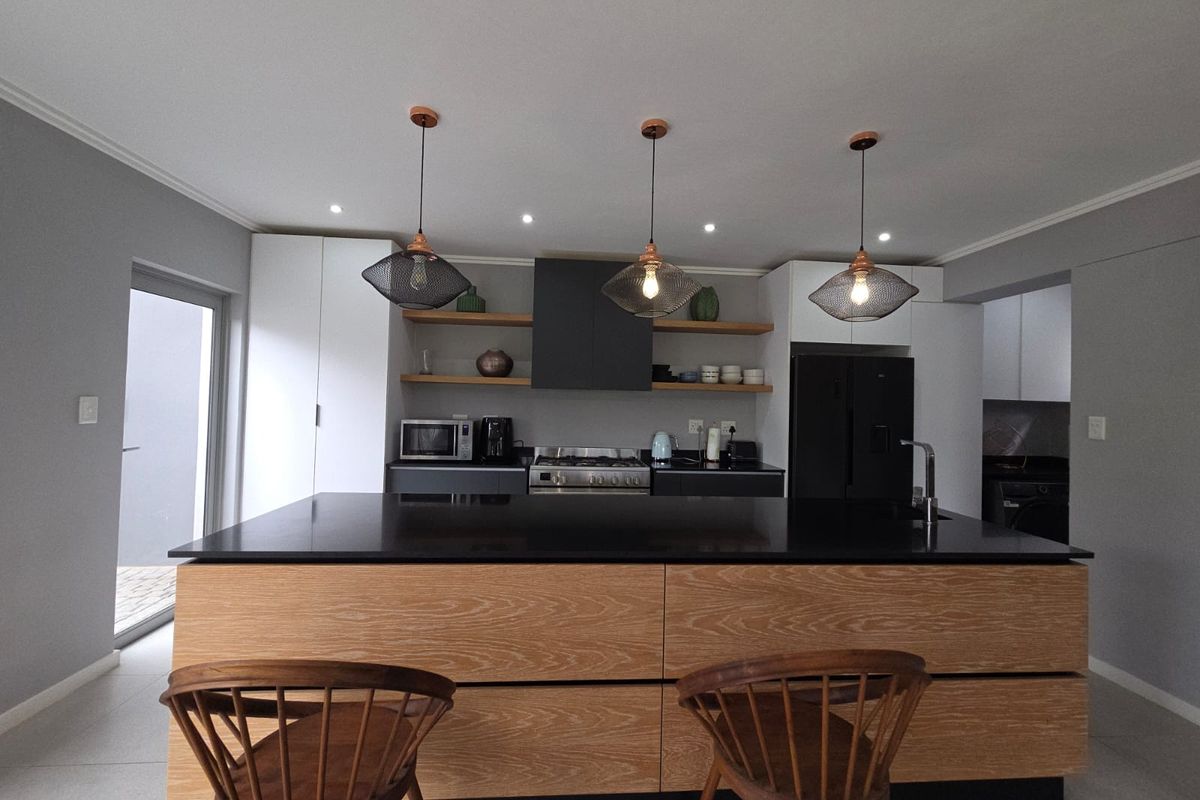 Modern kitchen featuring a large island with stone countertop, sleek cabinetry, floating shelves, and contemporary pendant lighting.