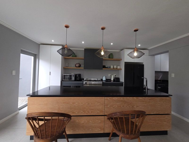 Modern kitchen featuring a large island with stone countertop, sleek cabinetry, floating shelves, and contemporary pendant lighting.