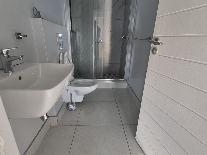 Modern bathroom featuring a wall-mounted basin, wall-hung toilet, and a glass-enclosed shower with neutral floor tiling.