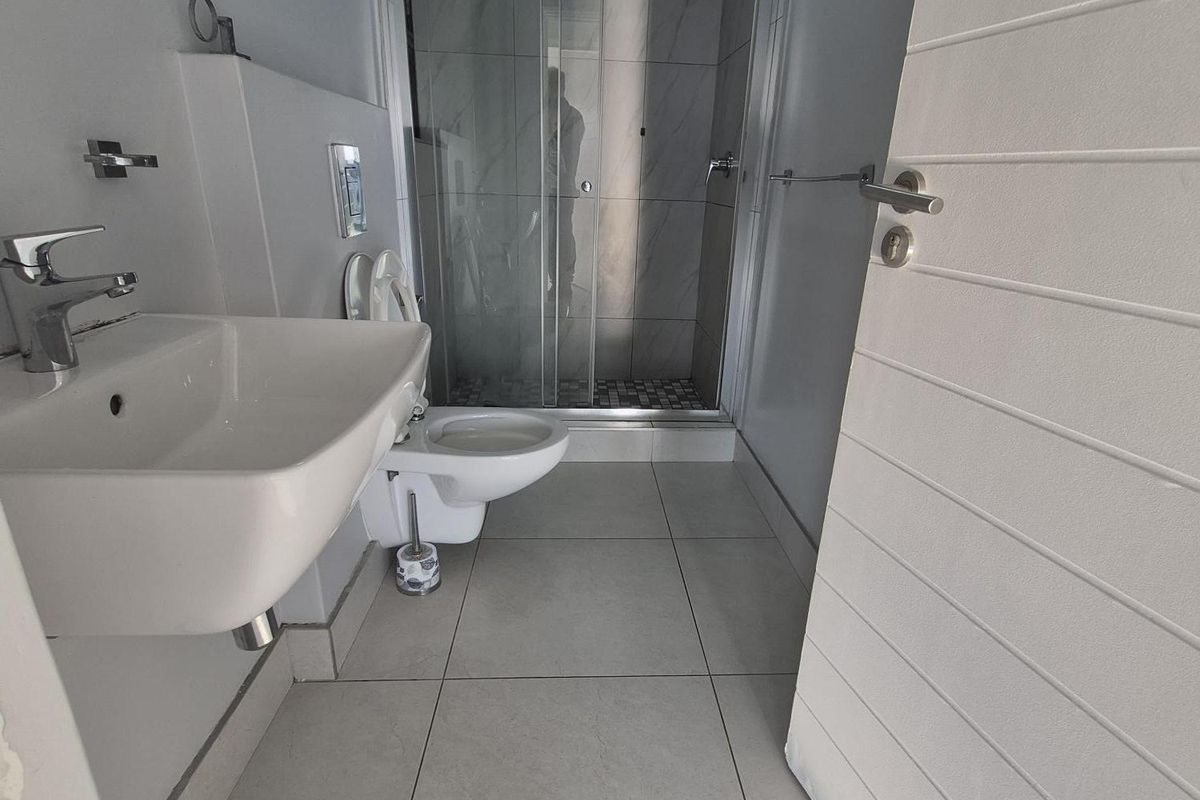 Modern bathroom featuring a wall-mounted basin, wall-hung toilet, and a glass-enclosed shower with neutral floor tiling.