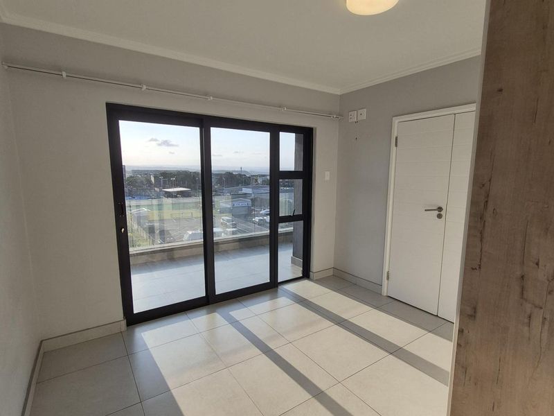 A bright, empty bedroom featuring modern tiled flooring, a flush mount ceiling light, and a large sliding glass door leading to a balcony.