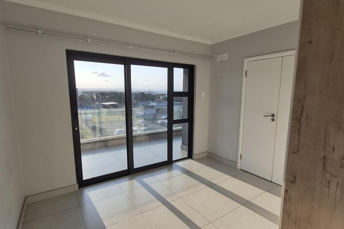 A bright, empty bedroom featuring modern tiled flooring, a flush mount ceiling light, and a large sliding glass door leading to a balcony.