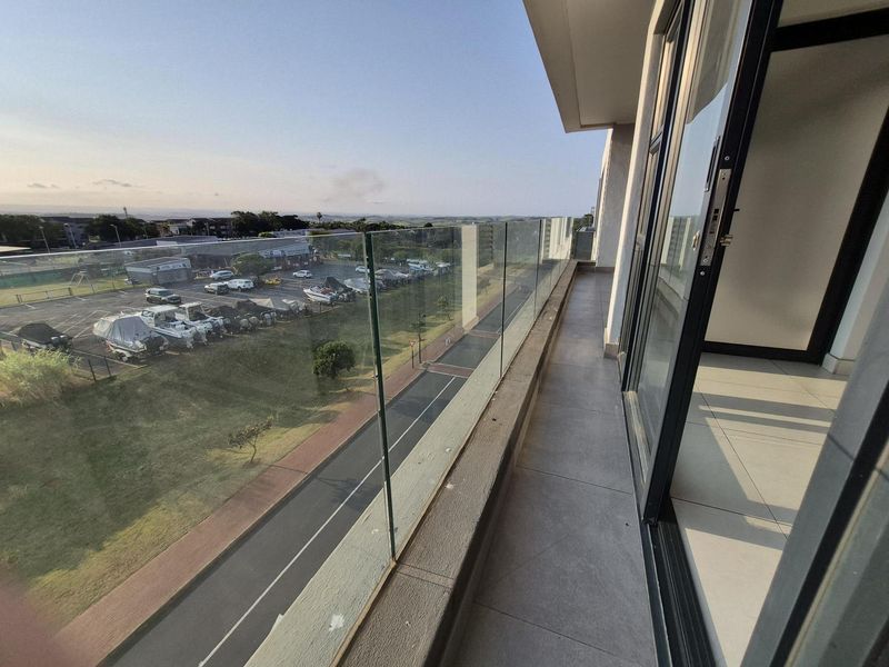 A modern balcony featuring a frameless glass balustrade, tiled flooring, and sliding door access, offering an elevated view of the surrounding area.