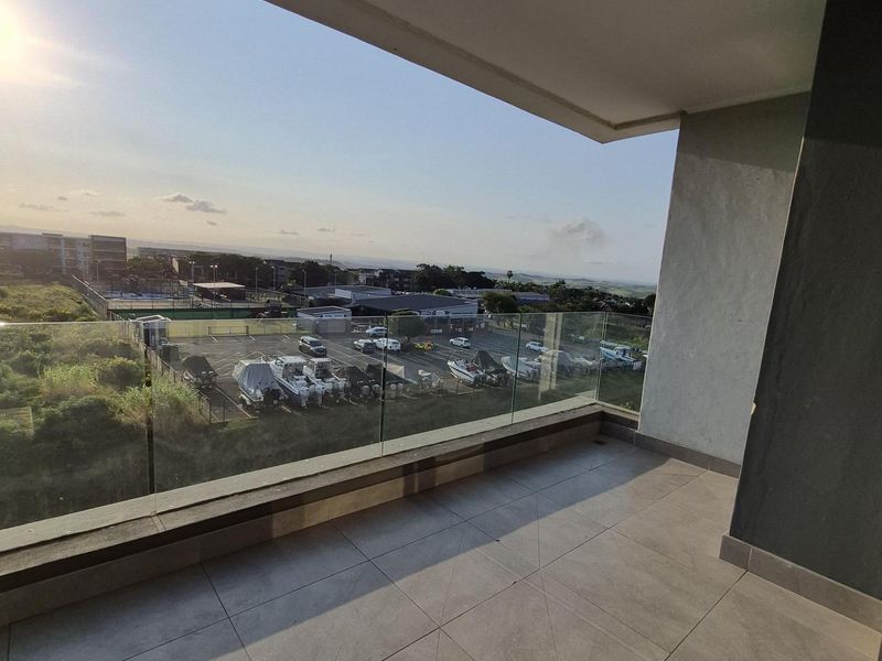 A spacious covered balcony featuring modern tiled flooring and a clear glass balustrade, offering an elevated view of the surrounding area.