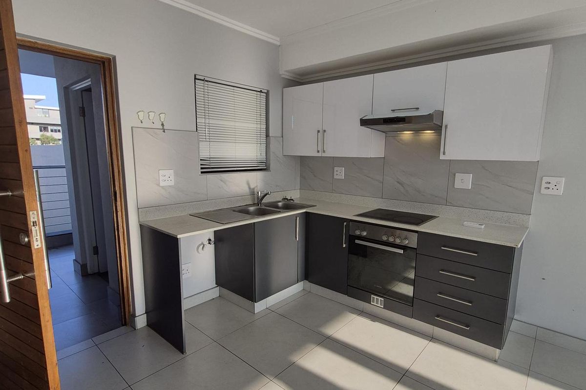 Modern kitchen featuring two-tone cabinetry, stone countertops, integrated oven and hob, and tiled flooring, offering a clean and functional workspace.
