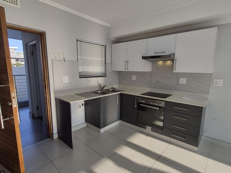 Modern kitchen featuring two-tone cabinetry, stone countertops, integrated oven and hob, and tiled flooring, offering a clean and functional workspace.