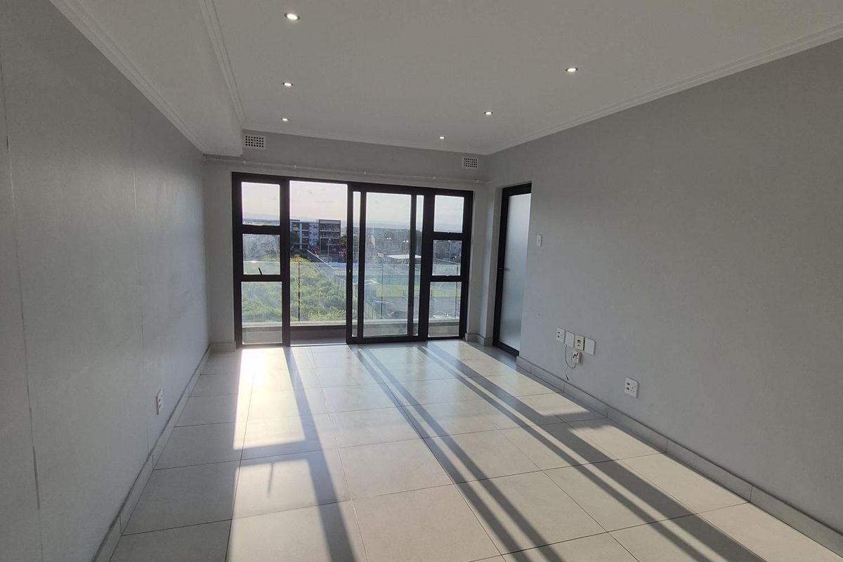 A bright, empty living area featuring neutral tiled flooring, recessed downlighting, and large sliding glass doors leading to an outdoor balcony.