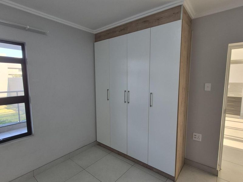 A bright, modern bedroom featuring neutral tiled flooring, a large built-in wardrobe with wood-grain accents, and clean, contemporary finishes.