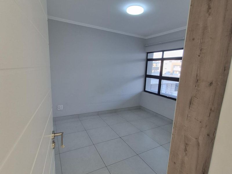 A clean, empty bedroom featuring neutral tiled flooring, modern aluminium window frames, and a bright recessed ceiling light, ready for personalization.