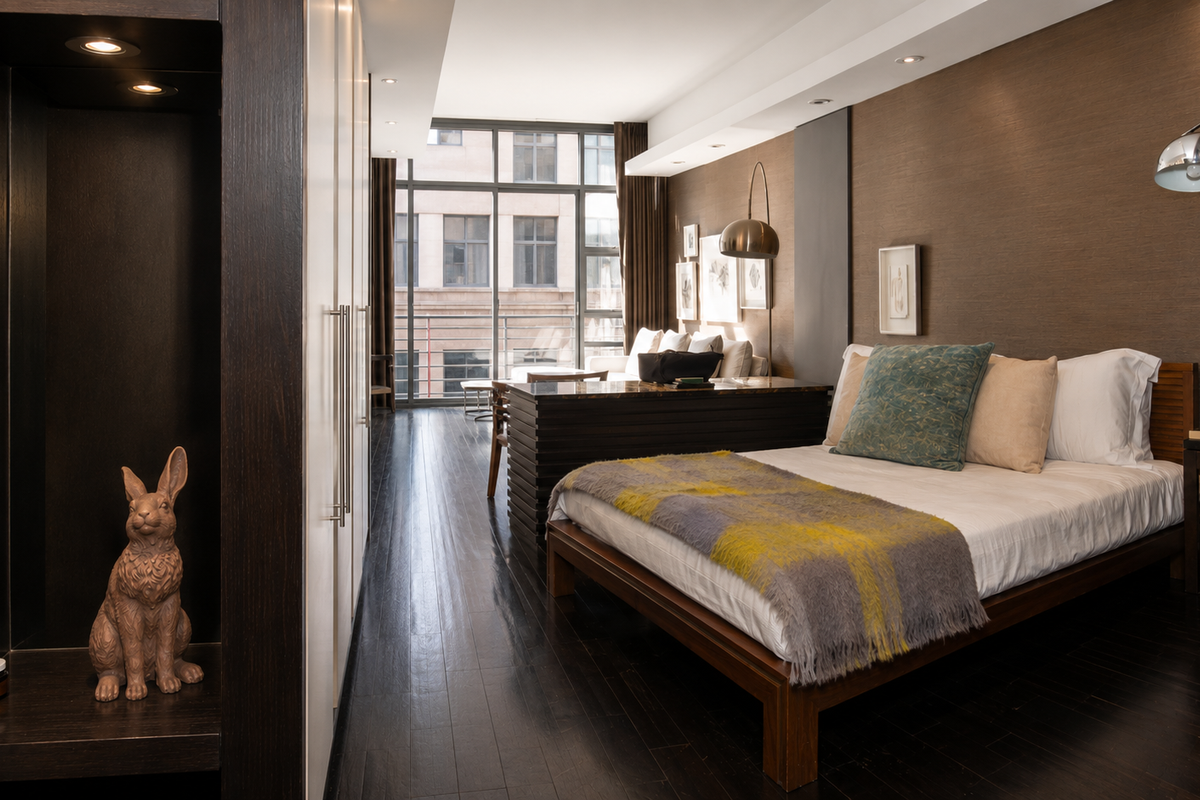 A well-appointed bedroom featuring dark hardwood flooring, built-in cabinetry, textured wall finishes, and large windows providing natural light and an urban view.