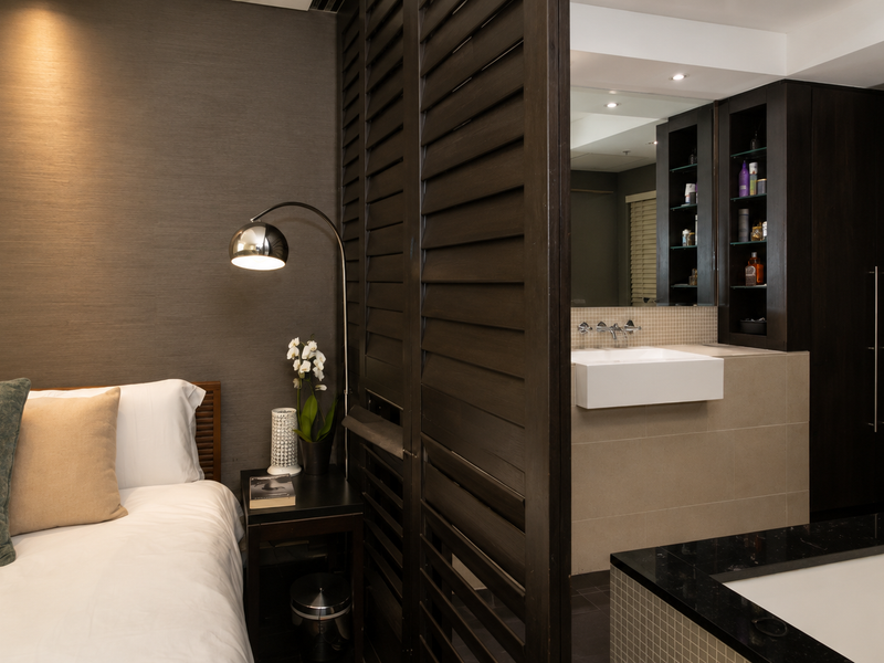 Modern bedroom featuring a semi-open ensuite bathroom with a vessel sink, built-in cabinetry, and a stylish slatted room divider.