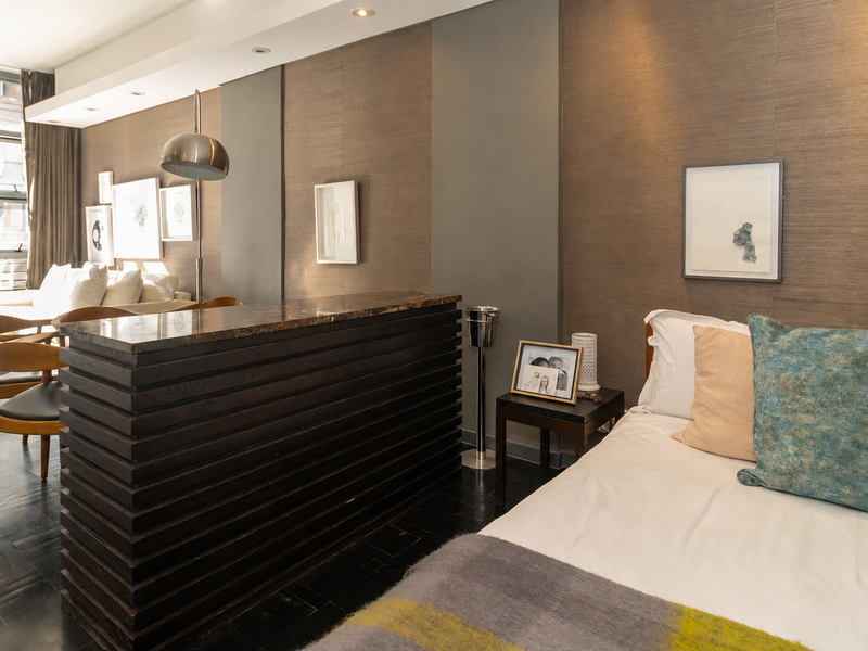 Modern open-plan living area featuring dark timber flooring, a custom built-in room divider with stone top, and large glass doors leading to a balcony.
