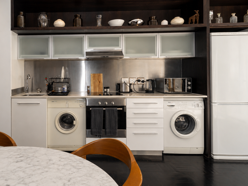 Modern kitchen featuring integrated cabinetry, stainless steel splashback, built-in oven, hob, extractor fan, and dedicated spaces for laundry appliances.