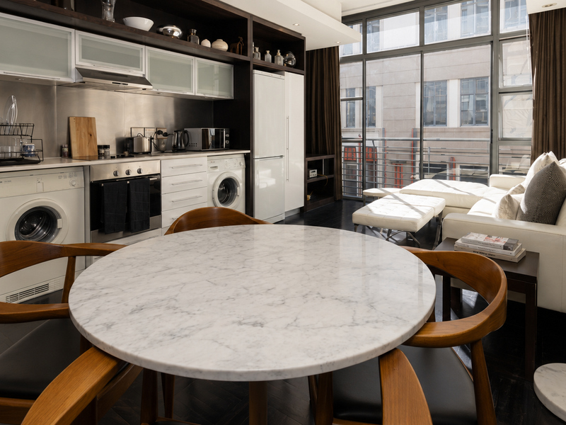 Modern open-plan living area featuring a sleek kitchen with integrated appliances, dark hardwood floors, and floor-to-ceiling windows providing ample natural light.