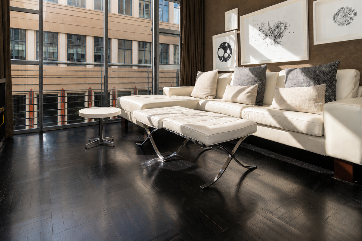 A modern living room featuring dark parquet flooring and large floor-to-ceiling windows that provide ample natural light and an urban view.