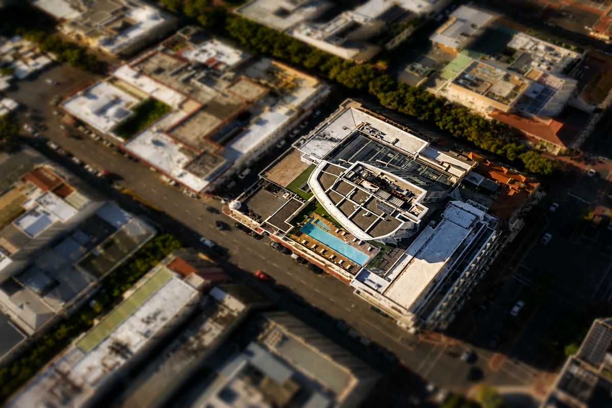 Aerial view of an apartment building featuring a rooftop swimming pool and terrace area in an urban setting.