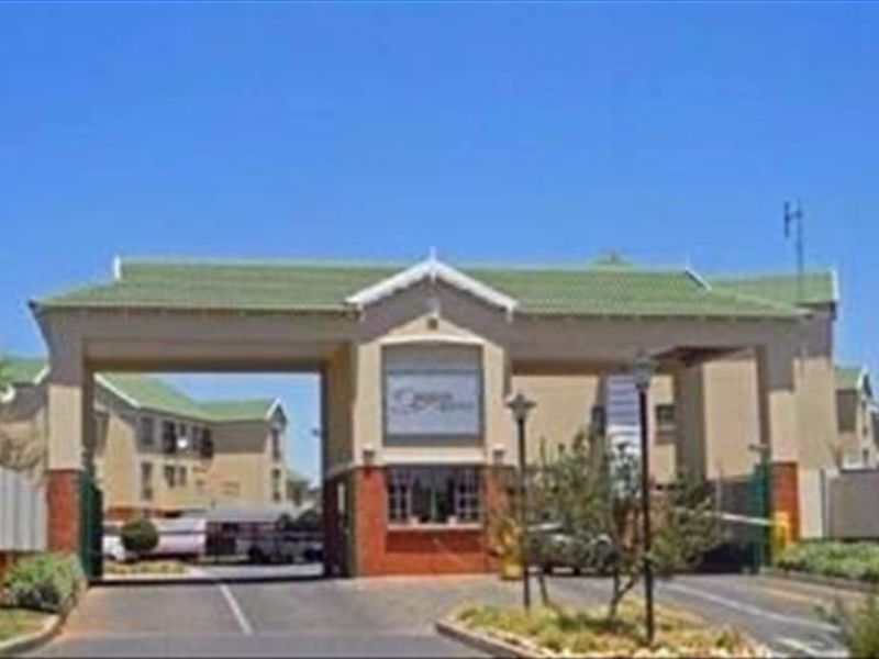 The main entrance and security gatehouse of the townhouse complex, featuring a tiled roof and controlled access boom gates.