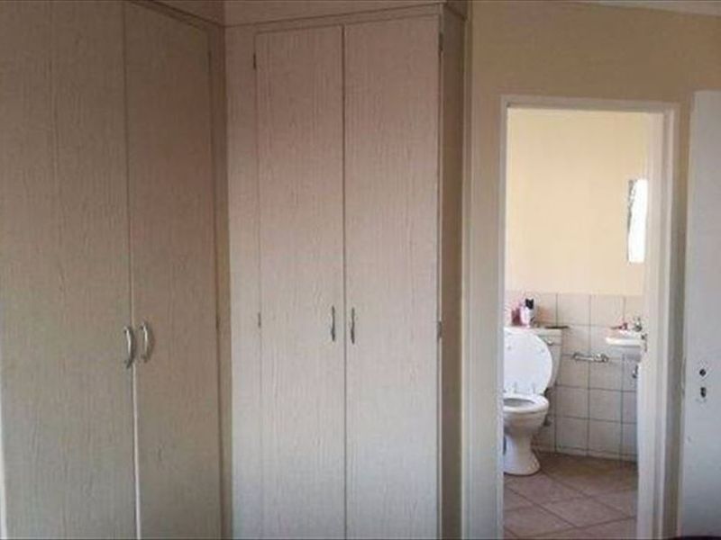 A bedroom featuring built-in cupboards with an adjacent en-suite bathroom visible through the doorway.