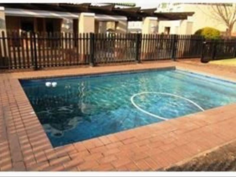A private swimming pool area featuring brick paving, a timber pergola, and secure perimeter fencing.