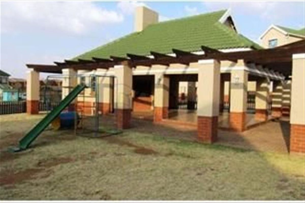 Rear view of the townhouse featuring a covered patio with a built-in braai, brick pillars, and a pergola structure overlooking the garden area.