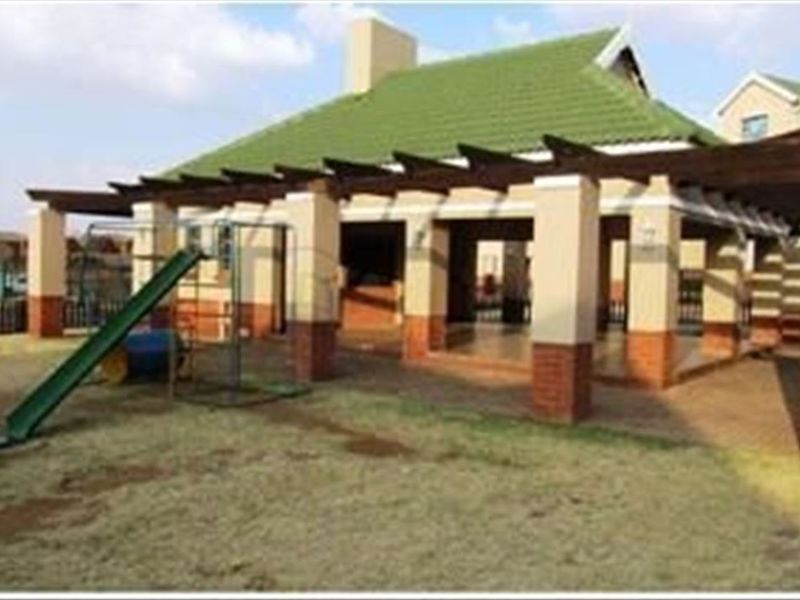 Rear view of the townhouse featuring a covered patio with a built-in braai, brick pillars, and a pergola structure overlooking the garden area.
