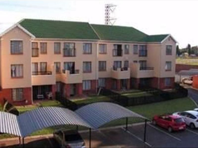 Exterior view of a multi-story townhouse complex featuring pitched roofs, private balconies, and covered parking bays within a landscaped residential estate.