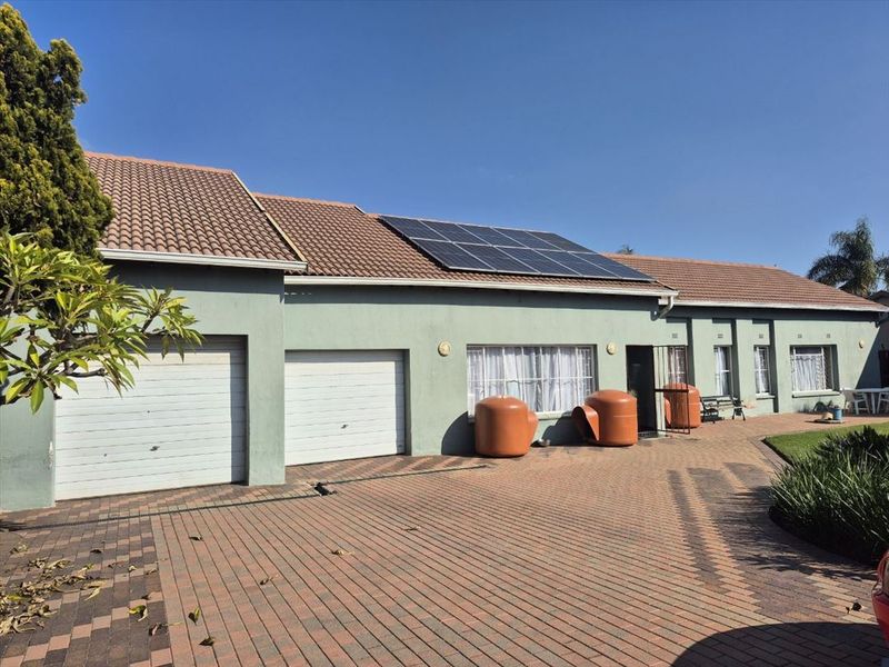 Front elevation of the property featuring a paved driveway, double garage, and roof-mounted solar panels under a clear sky.