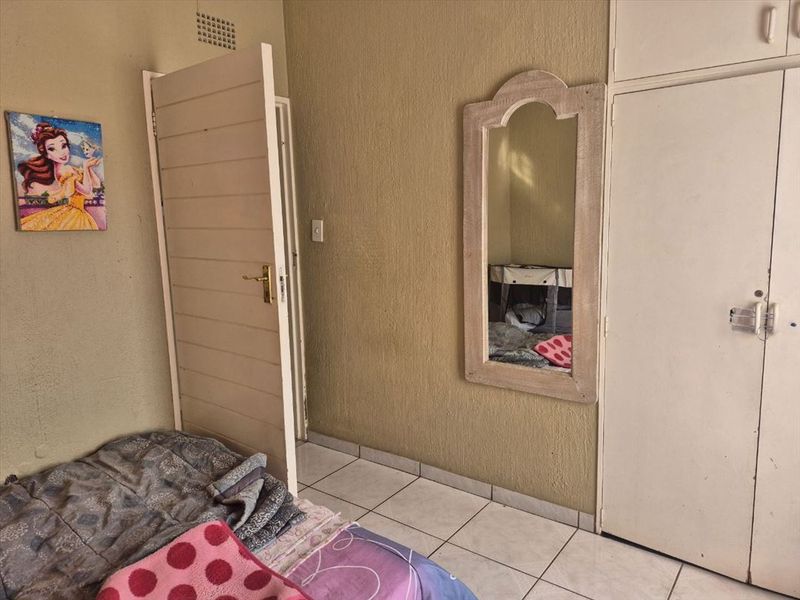 A bedroom featuring tiled flooring and built-in cupboards, requiring cosmetic updates to the wall finishes and general maintenance.