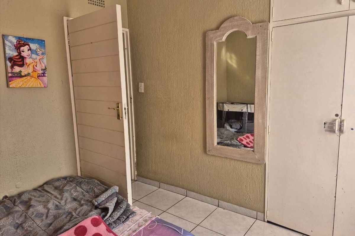A bedroom featuring tiled flooring and built-in cupboards, requiring cosmetic updates to the wall finishes and general maintenance.