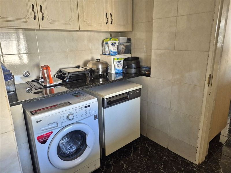 A functional laundry area featuring granite countertops, wall-mounted cabinetry, and durable ceramic wall and floor tiling.