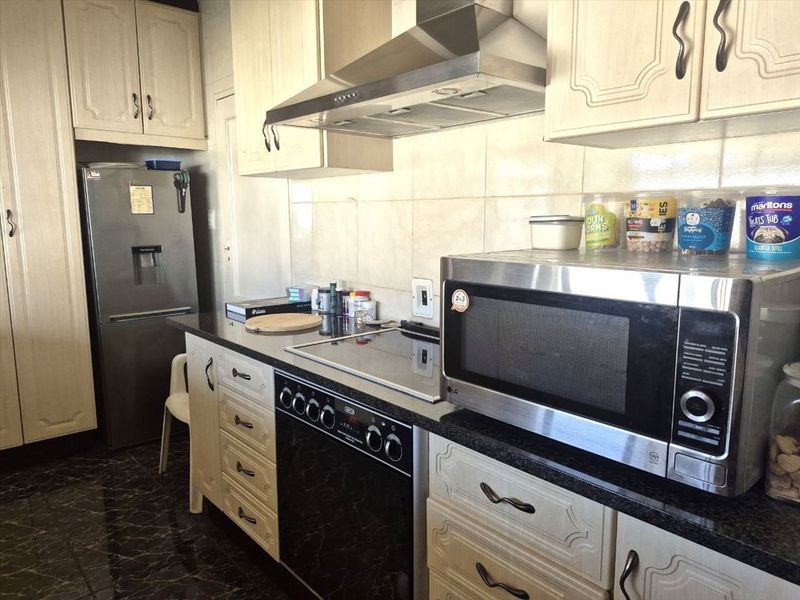 A functional kitchen featuring light-toned cabinetry, granite countertops, a tiled backsplash, and integrated cooking appliances including an electric hob and extractor fan.