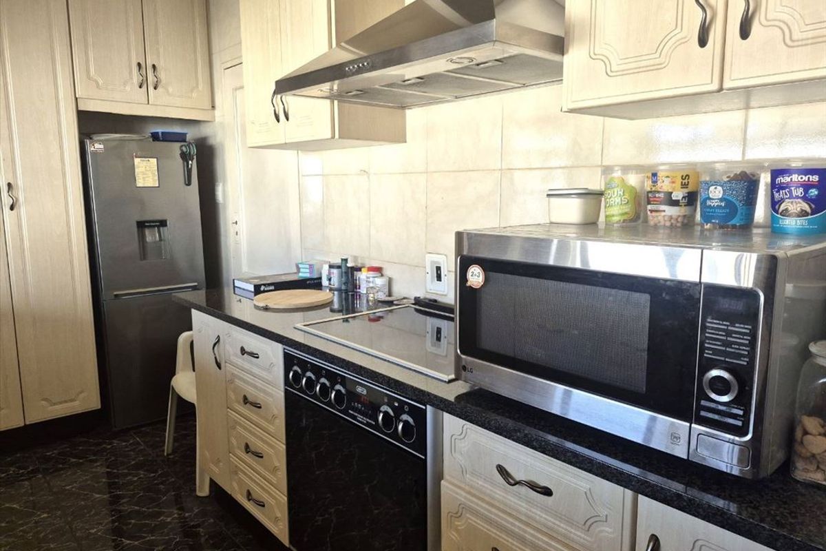 A functional kitchen featuring light-toned cabinetry, granite countertops, a tiled backsplash, and integrated cooking appliances including an electric hob and extractor fan.
