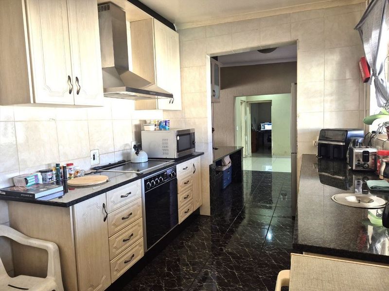 A functional kitchen featuring granite countertops, built-in cabinetry, a stainless steel extractor fan, and an integrated oven with tiled wall finishes.