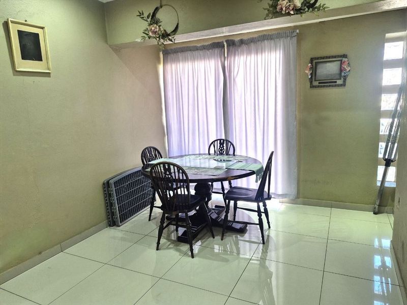 A dining area featuring light-colored floor tiles and a window with curtain treatments, providing a functional space for meals.