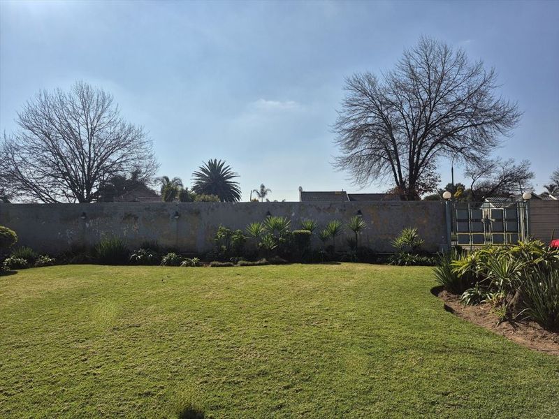 A spacious private garden featuring a well-maintained lawn, established landscaping, and a perimeter boundary wall with integrated lighting.