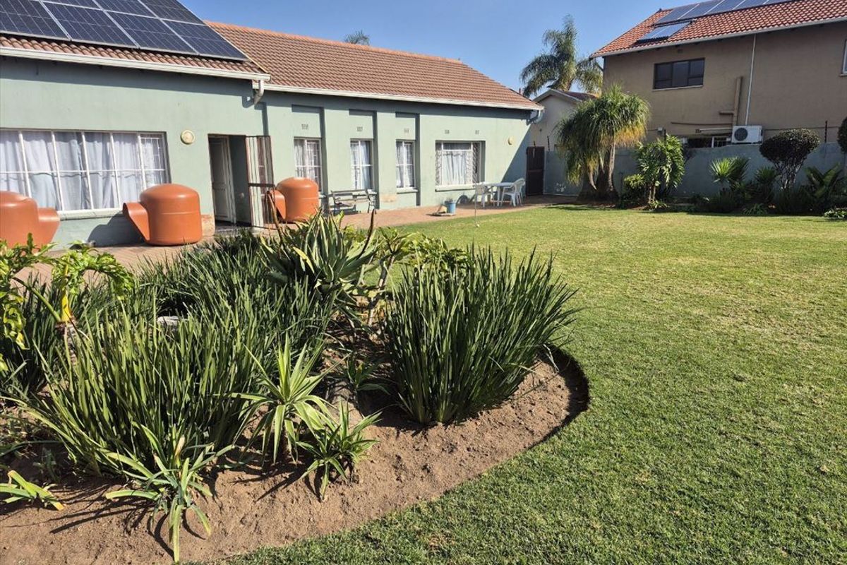 Spacious rear garden featuring a paved patio area, well-maintained lawn, established garden beds, and solar panels installed on the tiled roof.