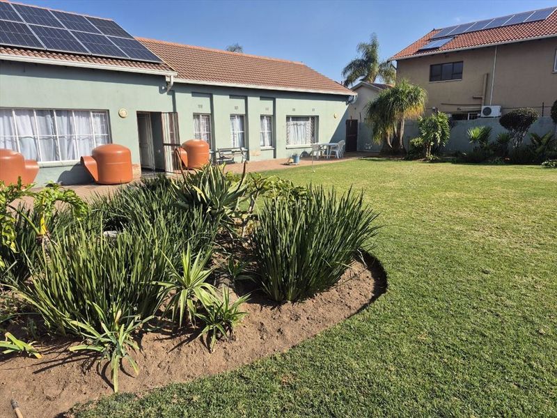 Spacious rear garden featuring a paved patio area, well-maintained lawn, established garden beds, and solar panels installed on the tiled roof.