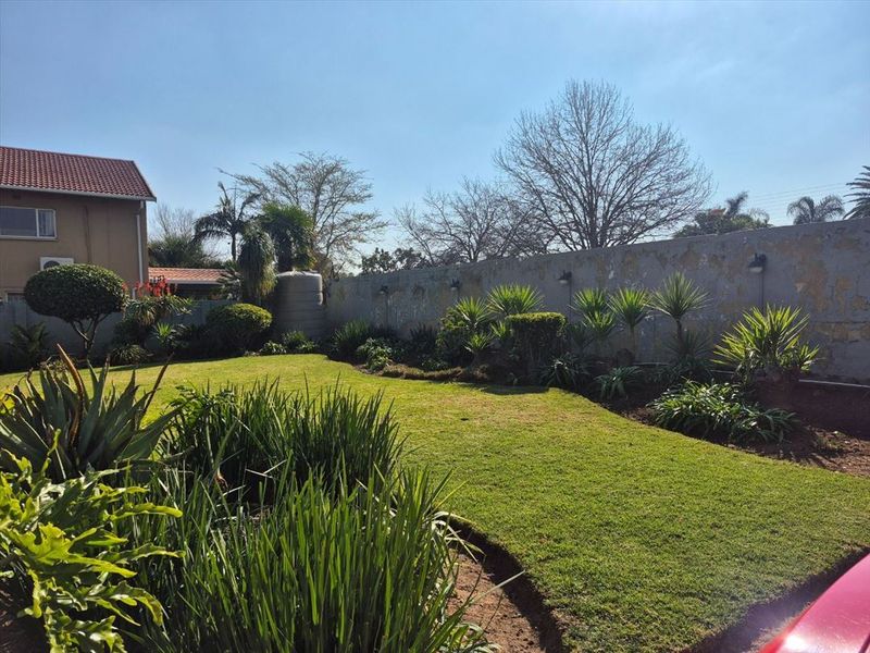 A well-maintained residential garden featuring a lush lawn, established landscaping, and a boundary wall with a water tank.