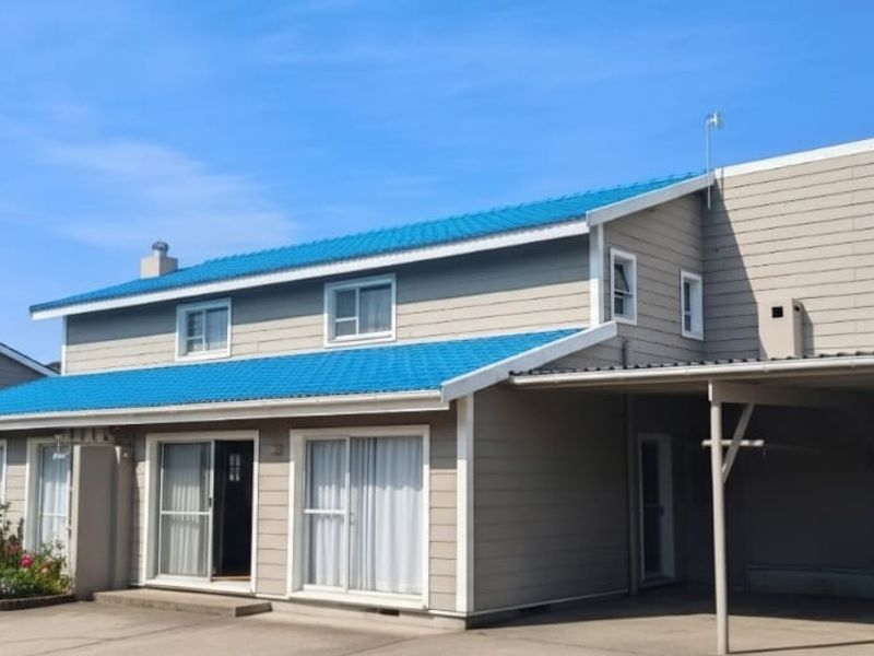 A two-story residential property featuring blue metal roofing, weatherboard cladding, and an attached carport with a concrete driveway.