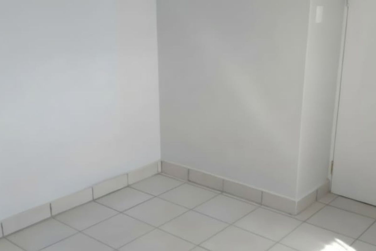 A clean, empty room featuring neutral white walls and light-colored tiled flooring with matching skirting boards.