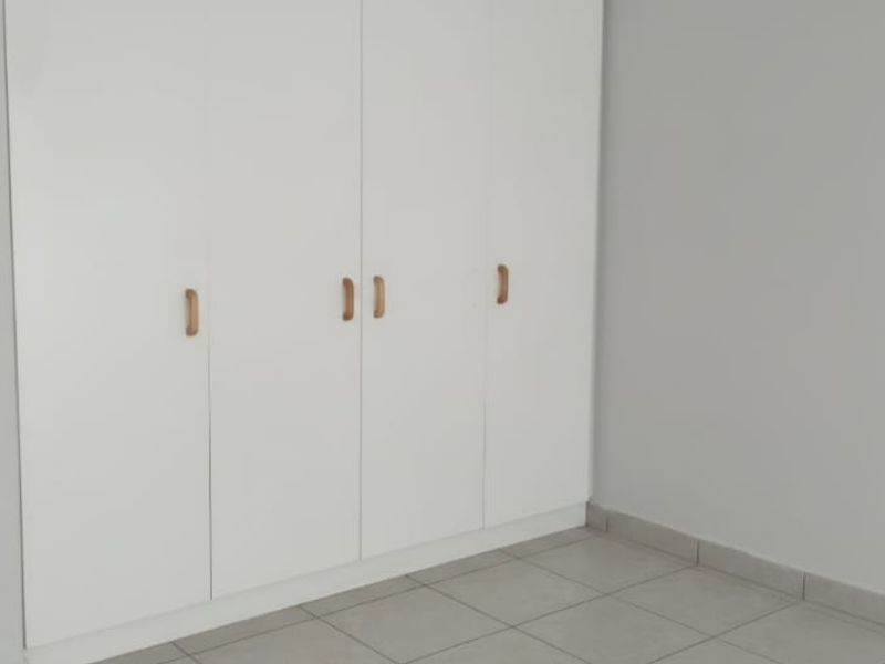 A clean, empty bedroom featuring neutral tiled flooring and modern white built-in cupboards with wooden handles.