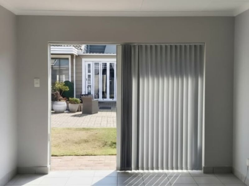 A bright, empty living room featuring neutral walls, tiled flooring, and a sliding glass door providing direct access to an outdoor patio area.