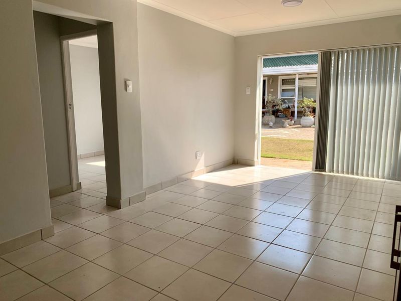 An empty, neutrally painted living room featuring ceramic floor tiles and a sliding glass door providing access to an outdoor patio area.